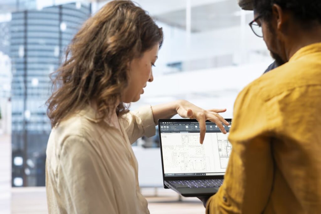 Two professionals collaborating over architectural plans displayed on a laptop screen in a modern office, illustrating the application of Human-Centric Design in workspace planning and user-focused innovation.
