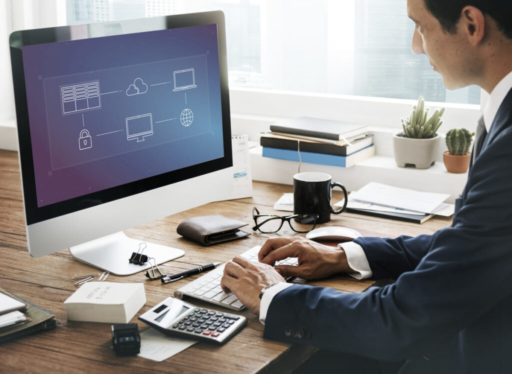 Business professional working on a desktop computer with a managed services network diagram displayed on the screen.