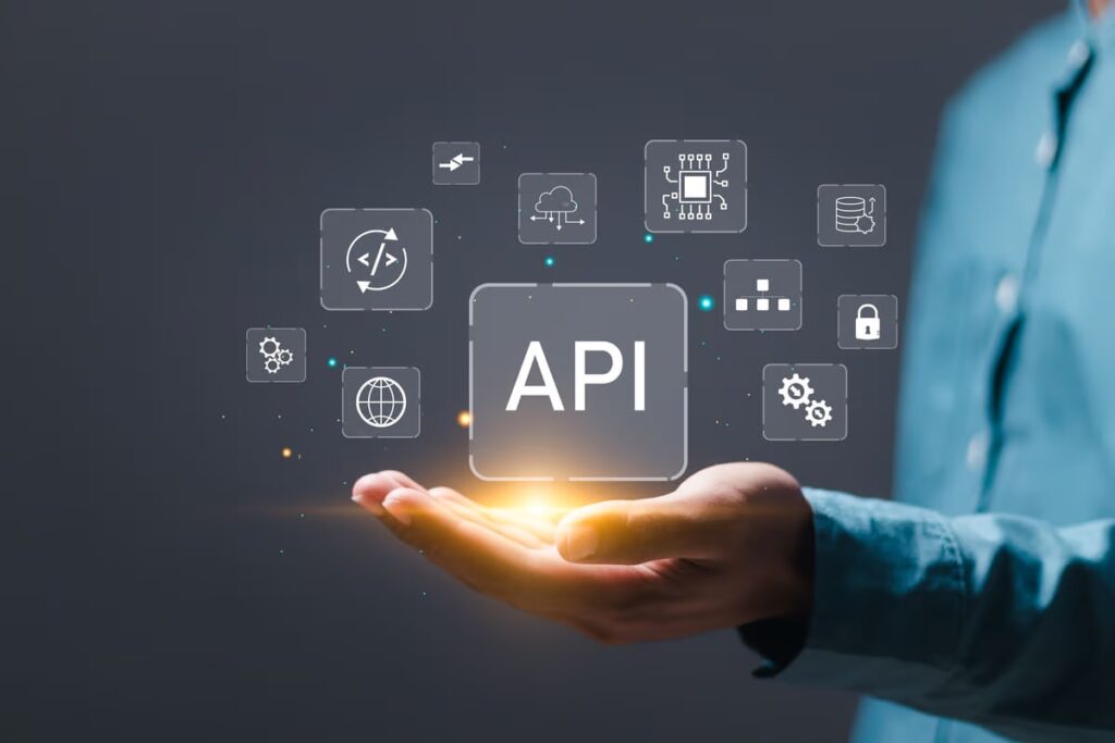 A business person's or developer's hand holds a virtual "API" icon floating above the palm. Surrounding it are technology icons such as code, cloud, and security, representing the concept of API integration to connect different software systems and applications.