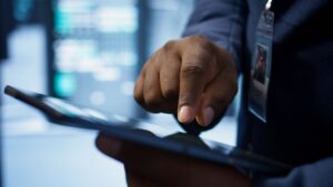 Close-up of a professional's hand interacting with a tablet in a secure, high-tech environment. This image represents the modern process of digital onboarding, where identity verification and user registration are handled efficiently through technology.