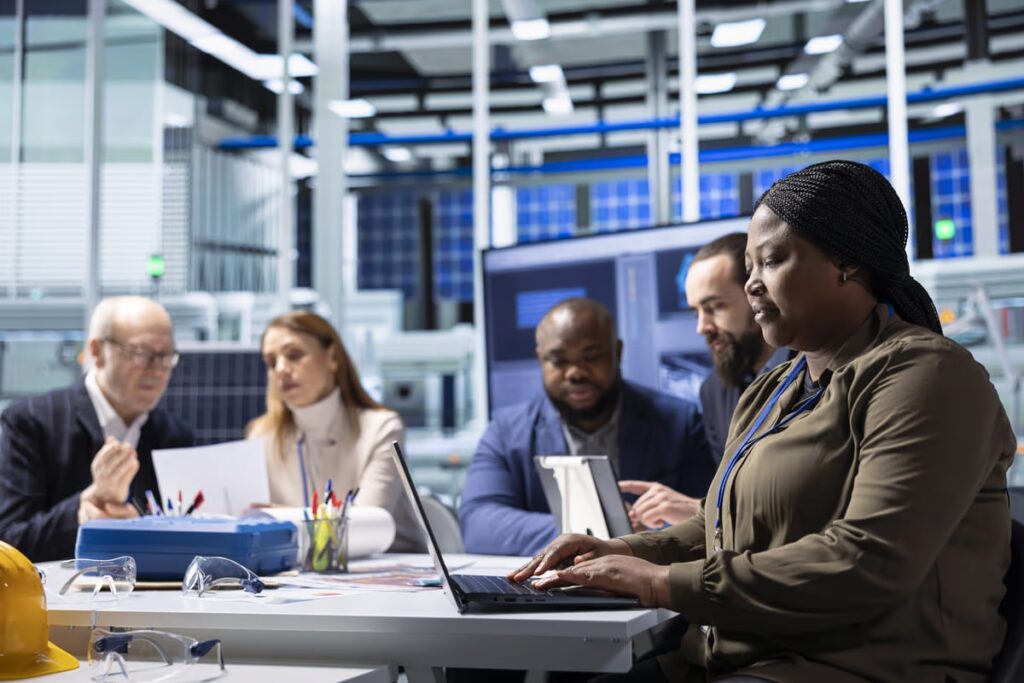 A diverse team of professionals in a high-tech facility engaged in an IT Service Management meeting, collaborating with laptops and documents to plan and oversee the delivery of technology services.