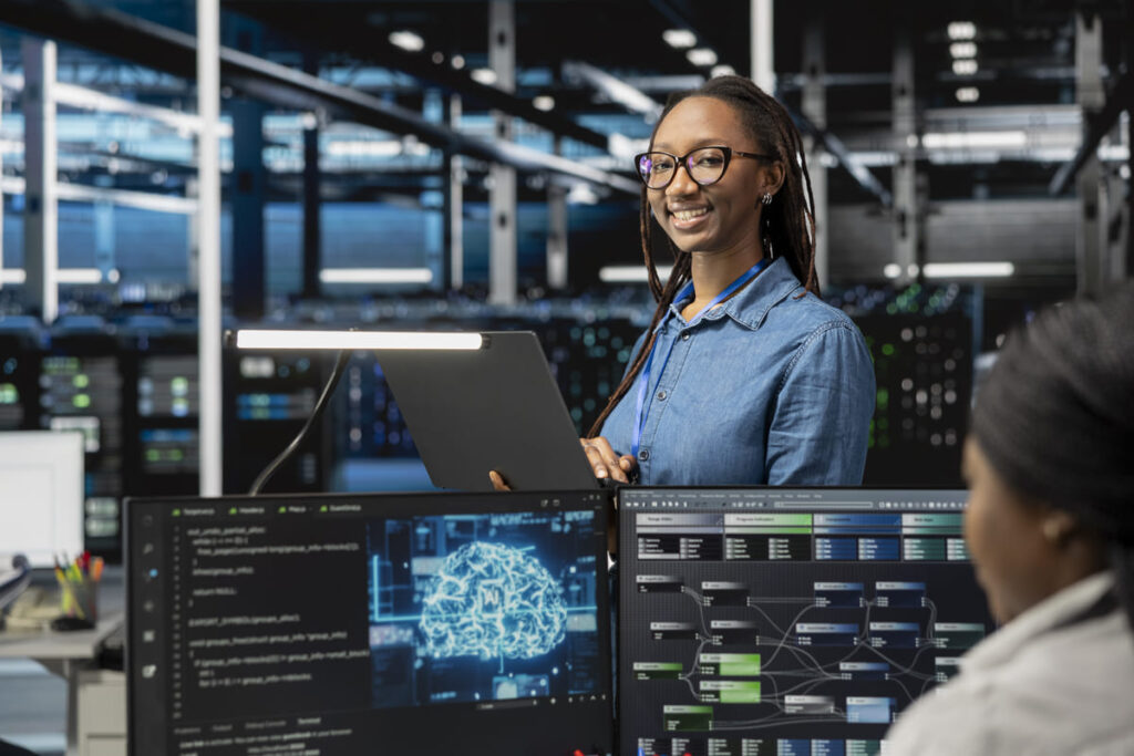 IT professional working in a modern data center while reviewing dashboards on two monitors, illustrating advanced workflows and the importance of system interoperability.