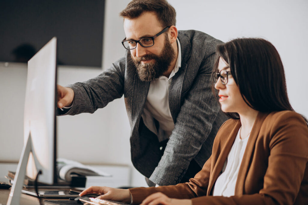 A male colleague pointing at a computer screen while collaborating with a female colleague, both using data to develop a customer centric business strategy.