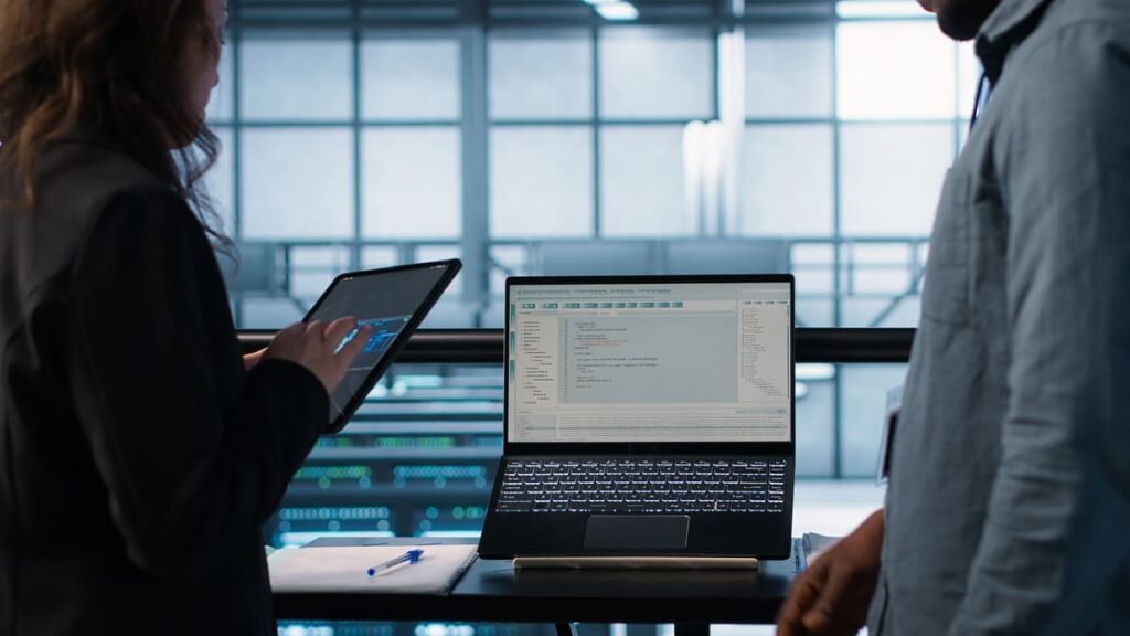Professionals analyzing system interfaces on a laptop and tablet in a tech environment, illustrating the technical process of platform implementation.