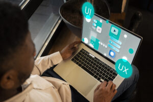 A man reviews a detailed user interface design on a laptop, with "UI" and "UX" bubbles, illustrating the focus on user experience.