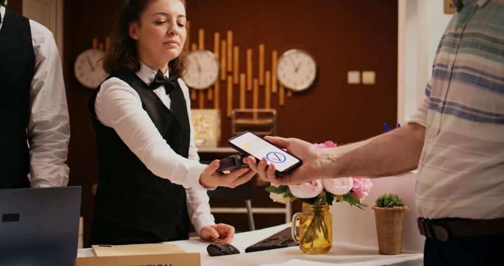 Hospitality technology solutions enabling a contactless smartphone payment between a guest and a receptionist at a hotel desk.