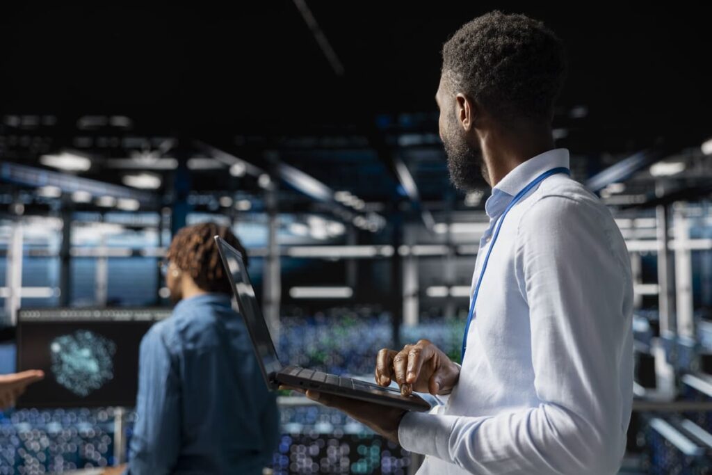 An IT professional holding a laptop in a modern data center embodies the core concepts of managed services, with server lights visible in the background.